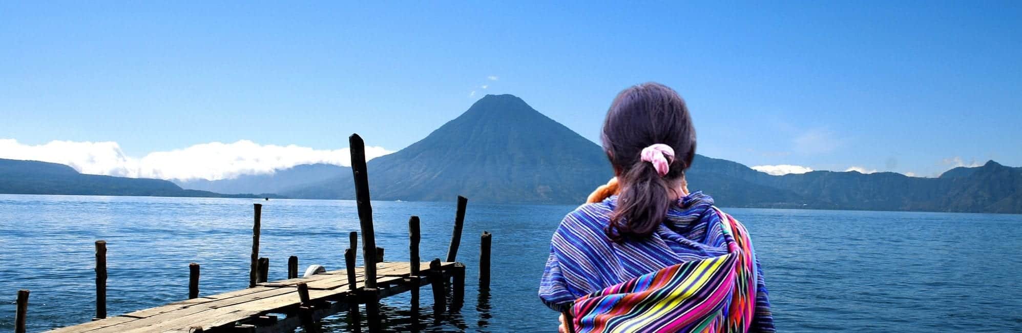 Maya-Mädchen steht am Ufer des Atitlán-Sees mit Blick auf Vulkan