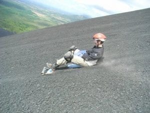 Tourist rutscht auf einem Board einen Hügel aus Vulkangestein hinunter